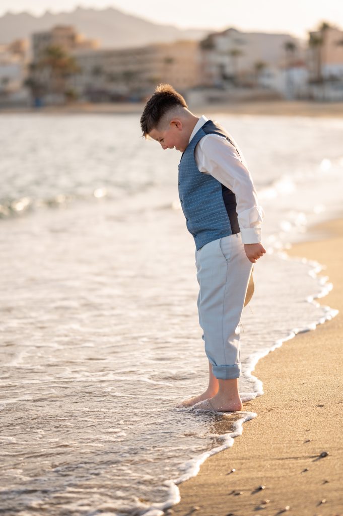 Niño con los pies en el agua caminando hacia el atardecer durante una sesión de fotos de comunión en la playa de Garrucha